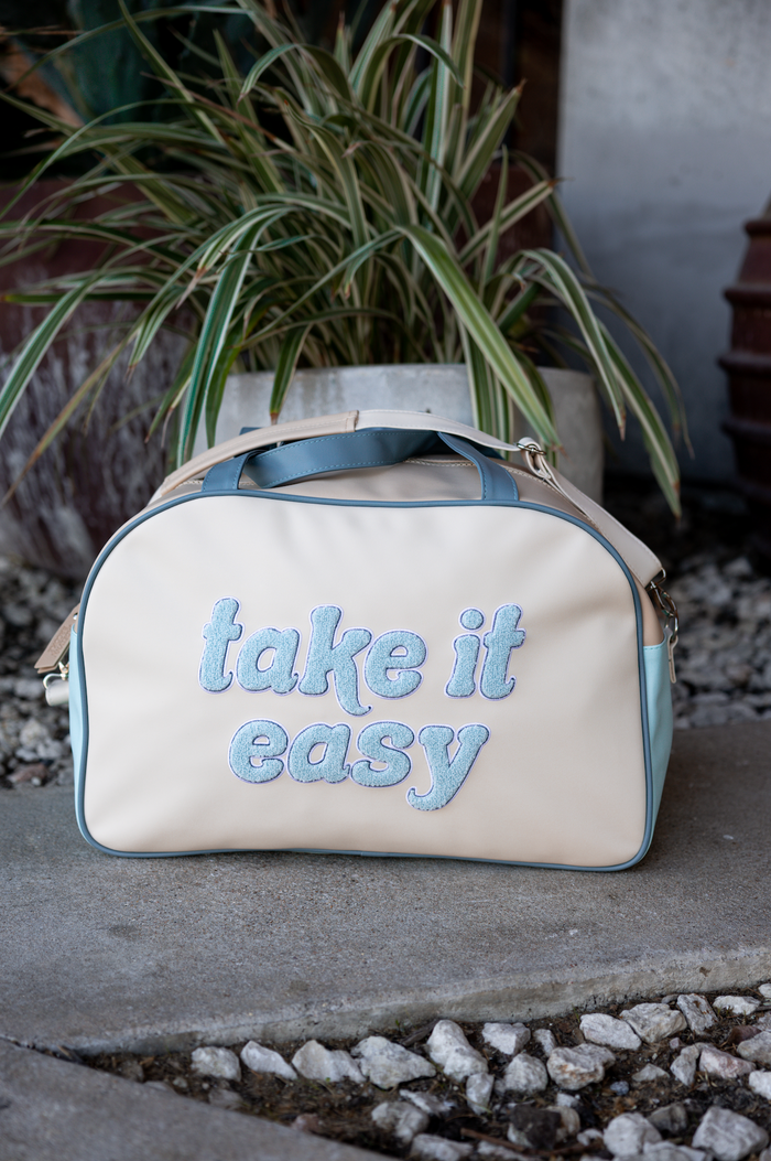 Beige and blue faux leather bag with 'take it easy' embroidery, perfect for casual outings.