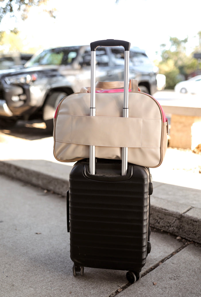 Beige travel bag atop a black carry-on suitcase with retractable handle, perfect for stylish travel.