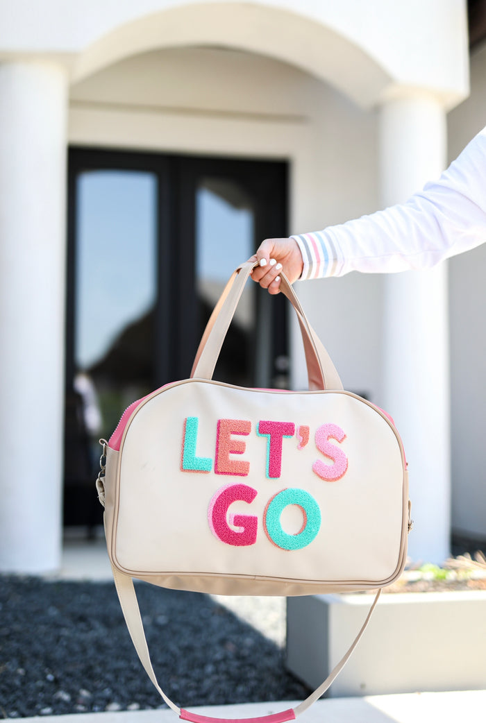 Beige travel bag with colorful 'LET'S GO' lettering, adjustable strap, and stylish design.