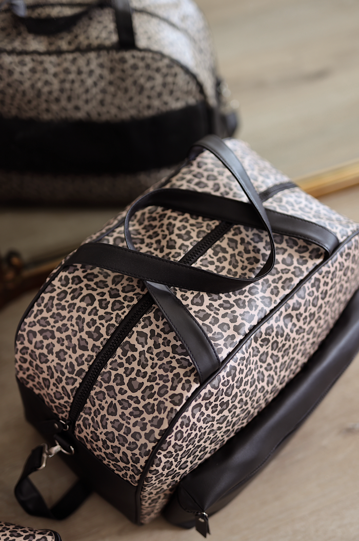 Leopard print duffel bag with black straps on a wooden surface