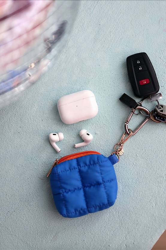 Blue quilted earbud case with AirPods and car keys on a light background.