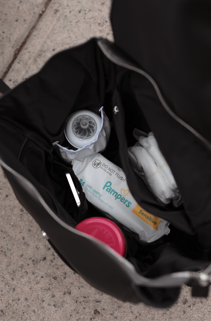 Black diaper bag with Pampers Sensitive wipes, baby formula container, and additional essentials inside.