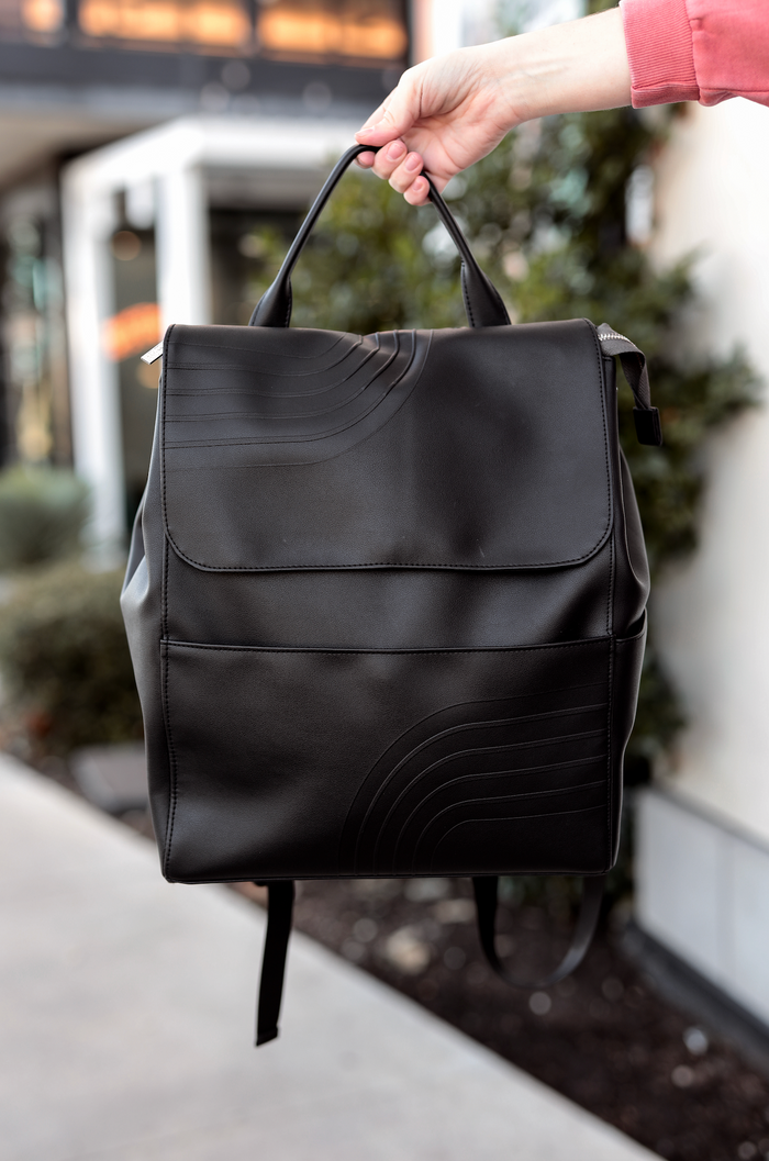 Stylish black leather backpack with minimalist design and textured wave details.