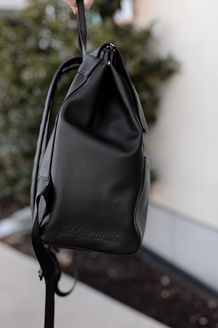 Stylish black faux leather backpack with logo, featuring adjustable straps and zippered closure.