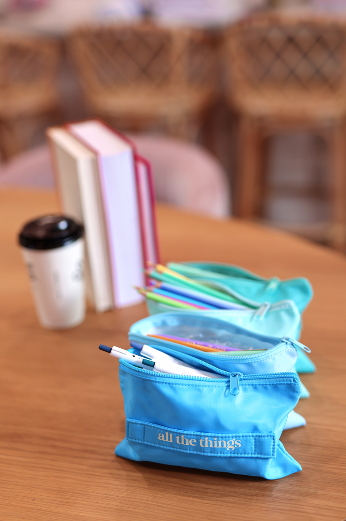 Turquoise fabric pencil case with white zipper, featuring colorful pens and markers, perfect for organization.