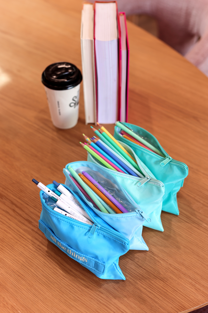 Set of turquoise pencil cases filled with colorful pens and pencils on wooden table.
