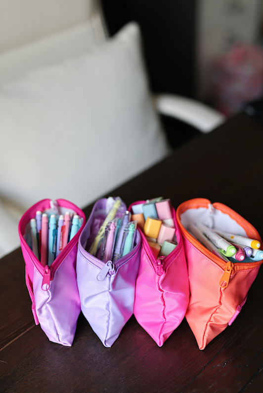 Vibrant zippered pencil cases in pink, purple, and orange, filled with colorful gel pens and sticky notes.