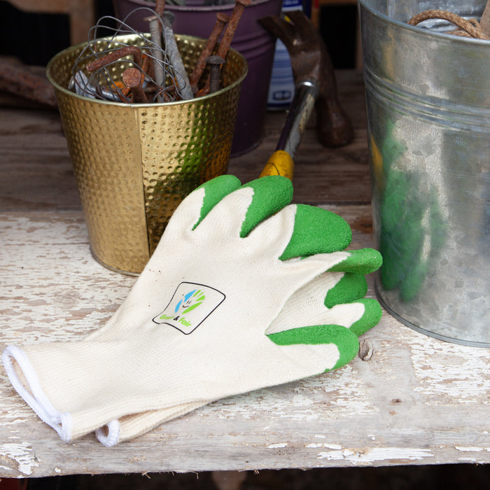 Gardening gloves with green fingertips on a wooden surface with gardening tools in the background.