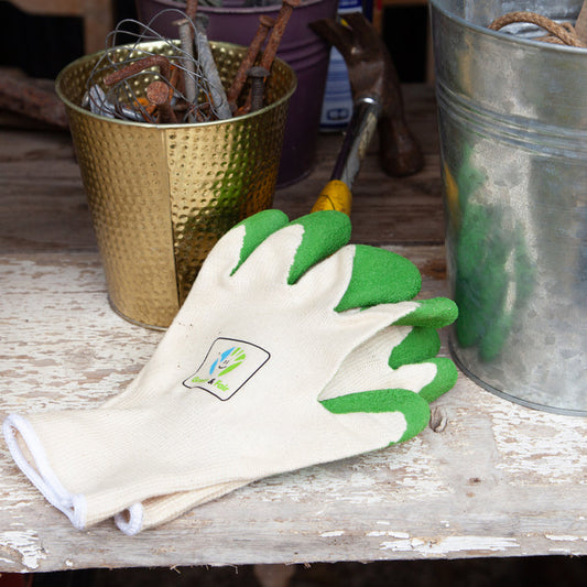 Gardening gloves with green fingertips on a wooden surface with gardening tools in the background.