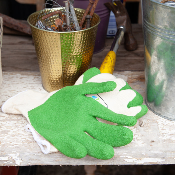 Green gardening glove on a wooden surface with tools and a gold pot in the background