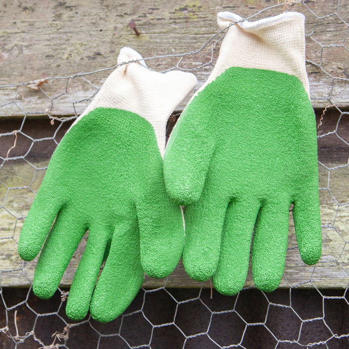 Pair of green gardening gloves on a wooden surface with chicken wire in the background