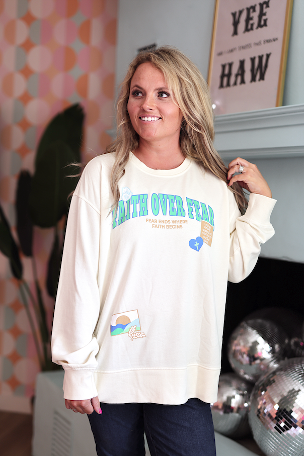 Cream oversized sweatshirt with 'Faith Over Fear' print and colorful graphic details.