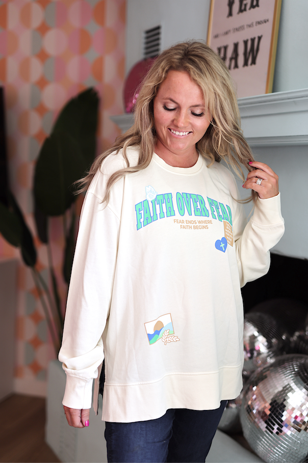 Cream oversized sweatshirt with 'Faith Over Fear' print, featuring unique graphics and relaxed fit.