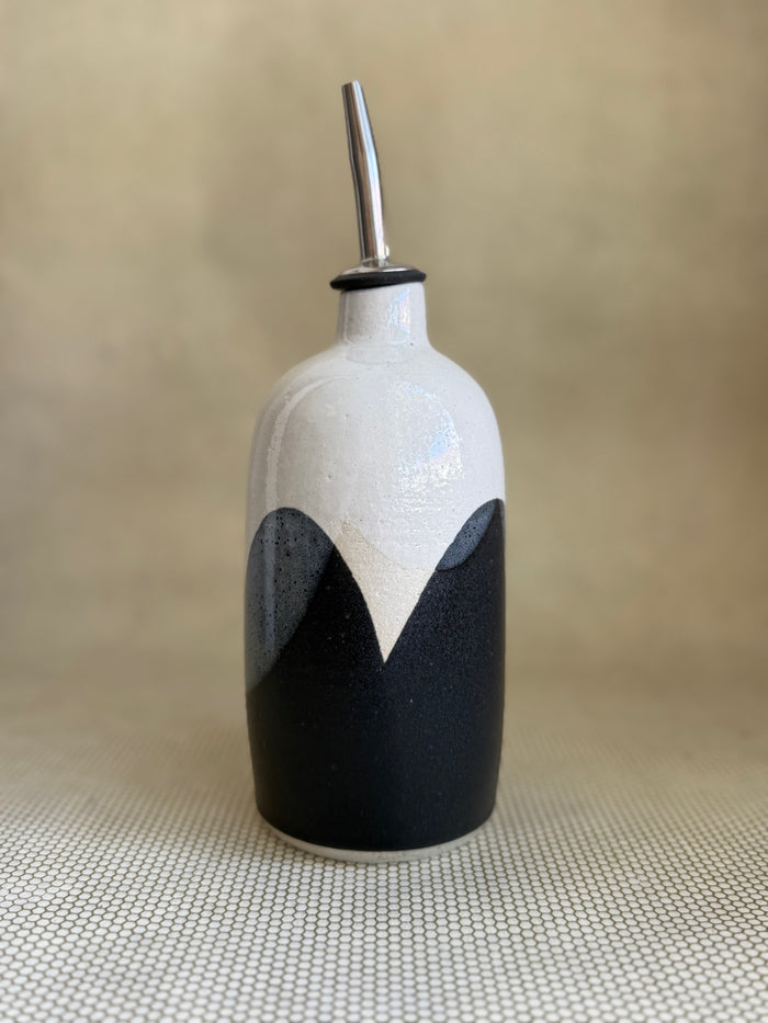 Ceramic oil cruet with black and white design on a beige background