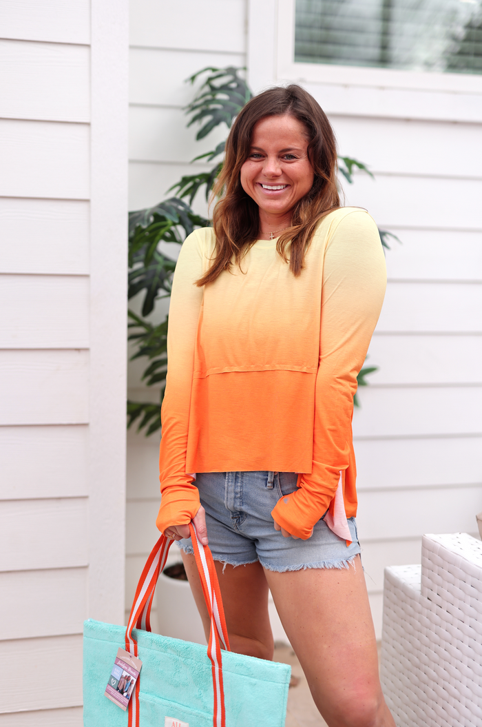 Women's ombre long sleeve shirt in orange and yellow with thumb holes, paired with denim shorts.