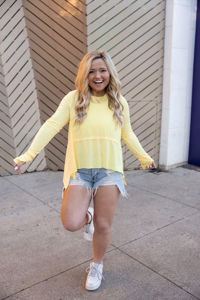Bright yellow long-sleeve top with a relaxed fit, paired with distressed denim shorts.