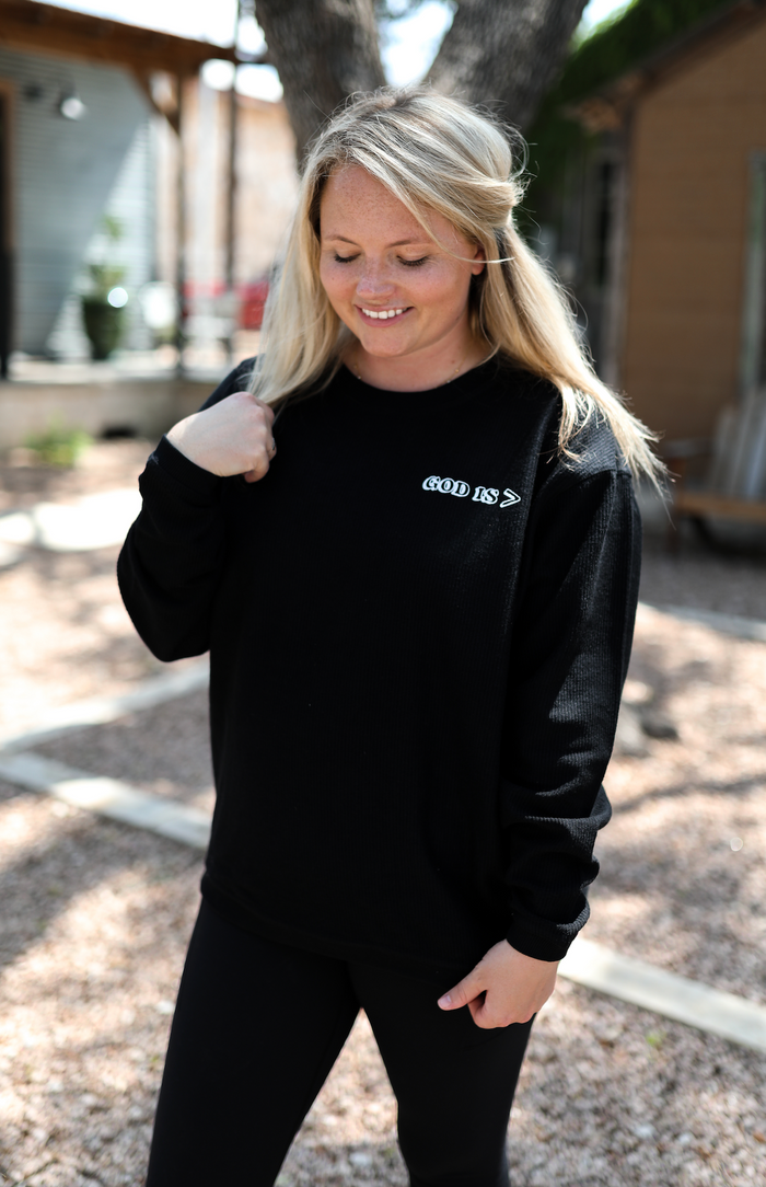 Black waffle knit sweatshirt with 'GOD IS >' design, perfect for casual, comfortable wear.