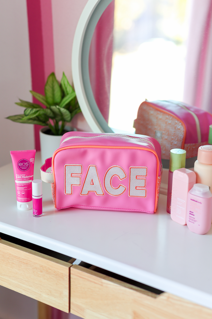 Pink cosmetic bag labeled 'FACE' with skincare products on a white vanity table.