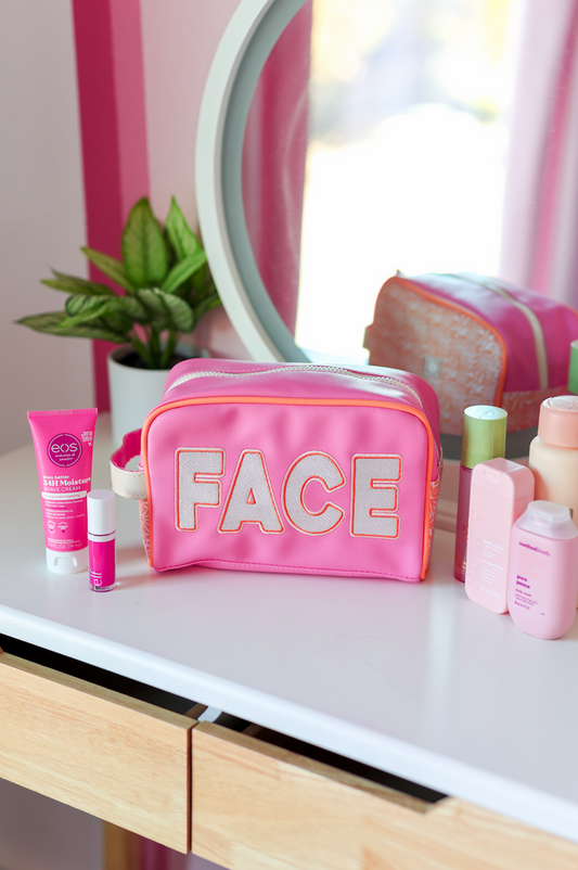 Pink cosmetic bag labeled 'FACE' with skincare products on a white vanity table.