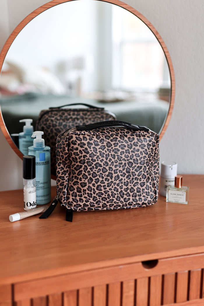 cheetah print makeup bag on a wooden dresser with mirror and skincare products.