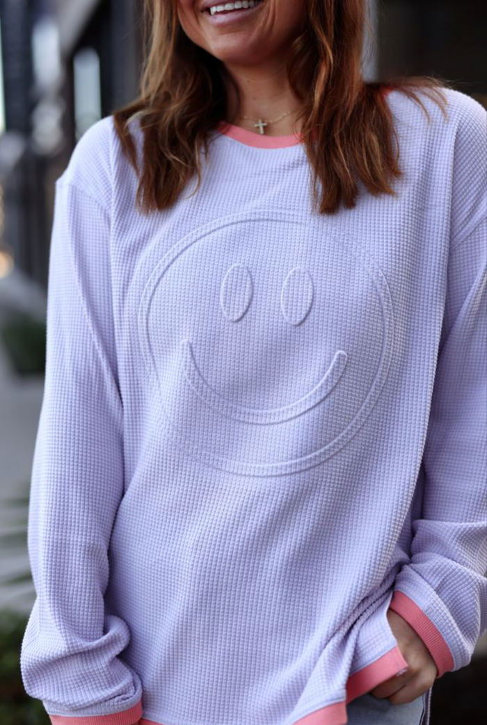 Cozy lavender smiley face sweatshirt with coral accents, perfect for casual wear.