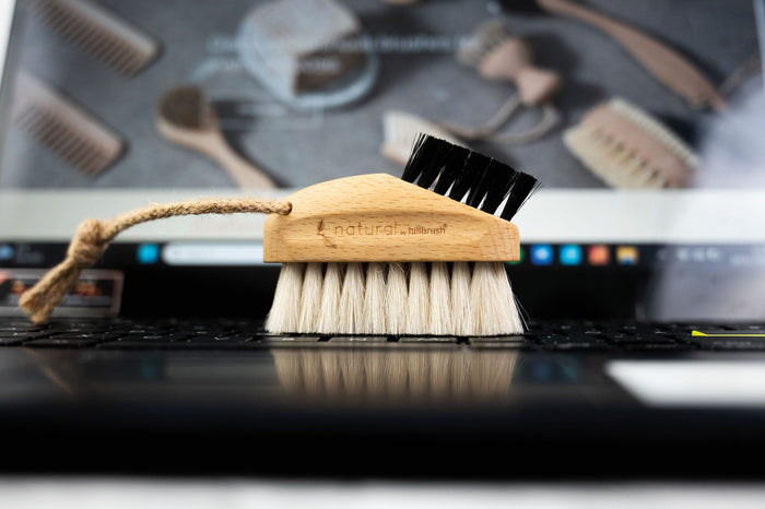 Hillbrush laptop brush on a laptop keyboard with a blurred background of cleaning tools.