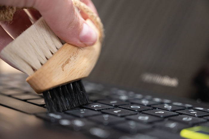 Person cleaning a laptop keyboard with a brush