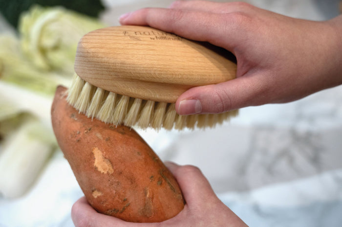 FSC timber and natural bristle vegetable scrubbing brush with two hands  to clean a sweet potato