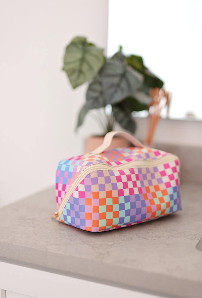 Colorful checkered cosmetic bag in pink, purple, and orange with a zipper and handle for easy carrying.