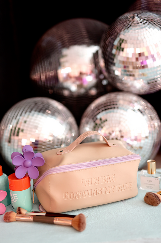 Stylish pink makeup bag with zipper and embossed text, featuring cosmetic brushes and items around it.