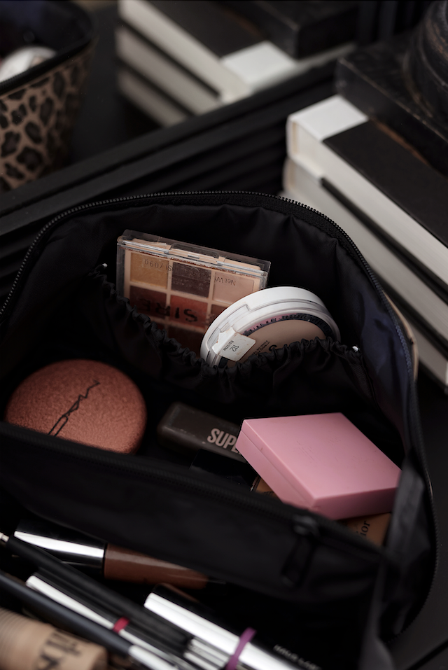 Black cosmetic bag filled with makeup products including blush, powders, and lipsticks.