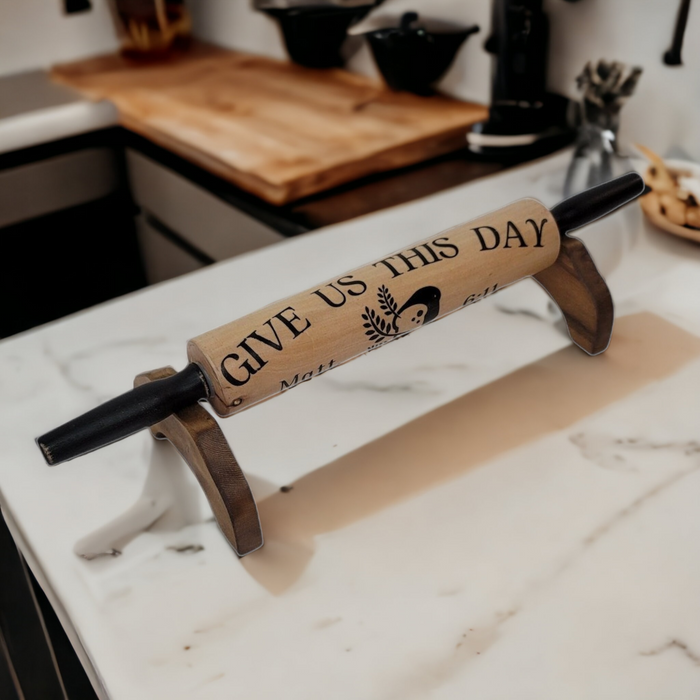A wooden rolling pin with an engraved message 'Give Us This Day Our Daily Bread' placed on a kitchen counter.