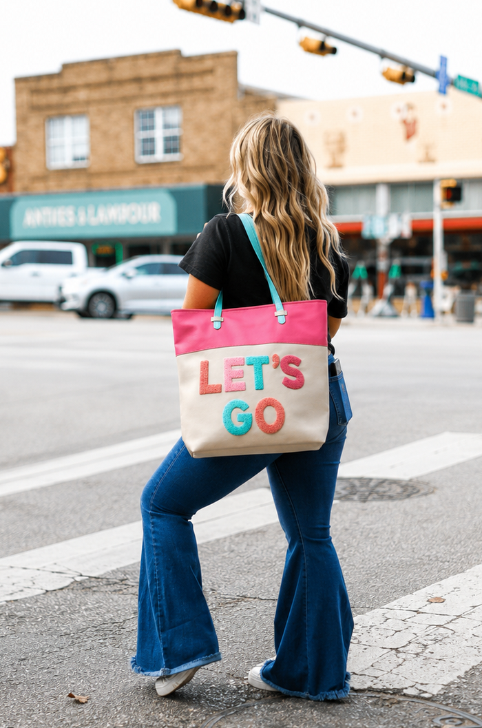Woman carrying a tote bag with 'LET'S GO' text on a city street.