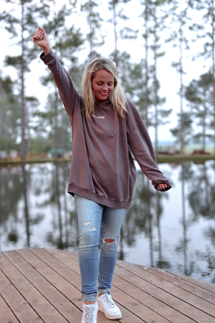 Cozy oversized brown hoodie with 'live boldly' text, paired with ripped blue jeans and white sneakers.