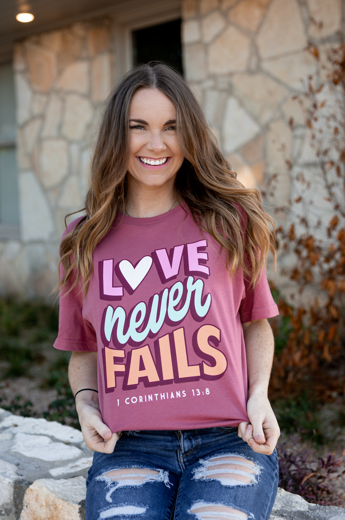 Maroon graphic tee reading 'Love Never Fails,' made of soft cotton, perfect for casual wear.