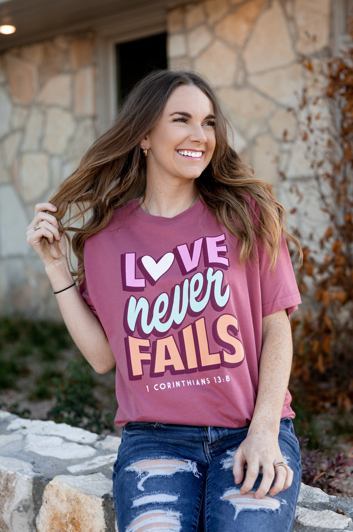 Maroon graphic t-shirt with 'Love Never Fails' design, casual fit, perfect for everyday wear.