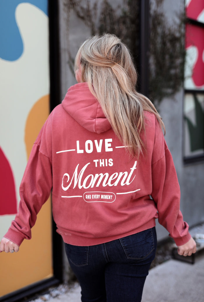 Cozy coral hoodie with 'Love This Moment' graphic on back, perfect for casual wear and comfort.