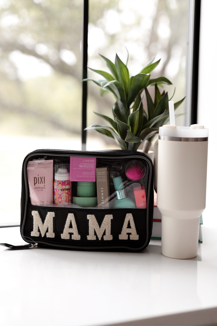 Black zippered cosmetic bag with 'MAMA' letters, filled with skincare products and a tumbler beside it.