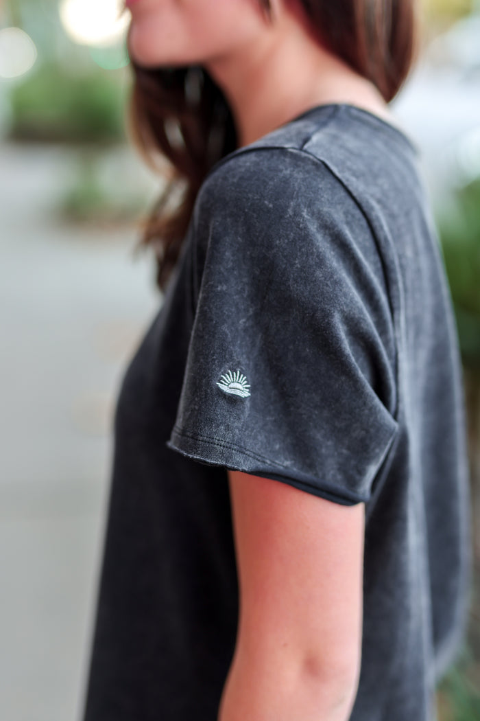 Side view of a women's charcoal gray t-shirt made of soft cotton with a sunburst embroidered detail.