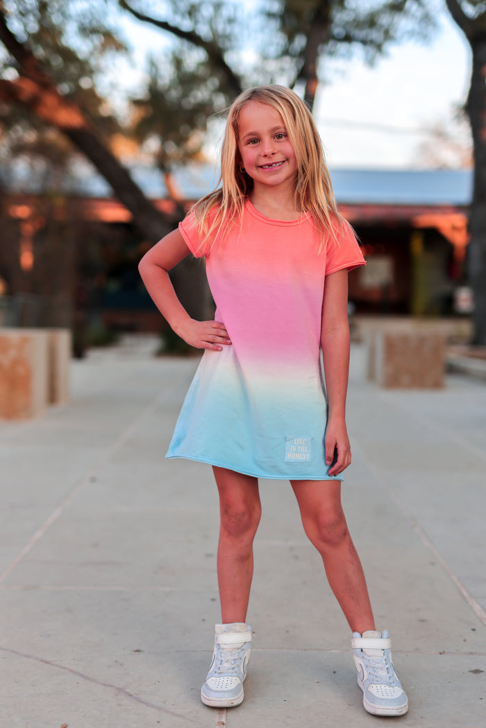 Young girl wearing a colorful dress standing on a sidewalk with trees in the background
