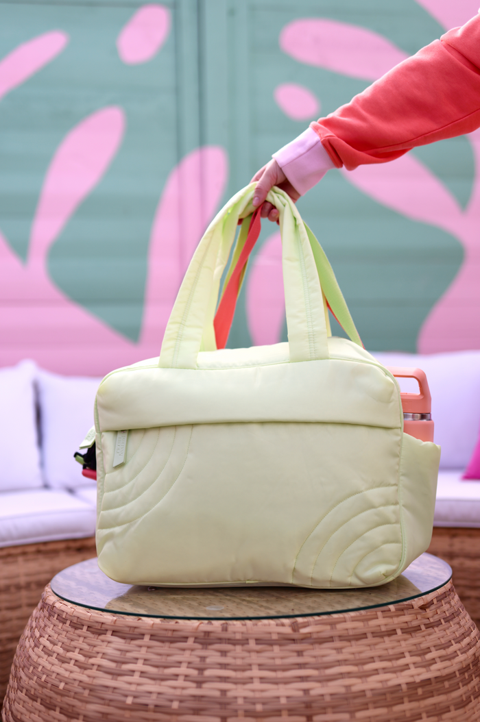 Light green padded tote bag with multicolor straps, perfect for stylish on-the-go storage.