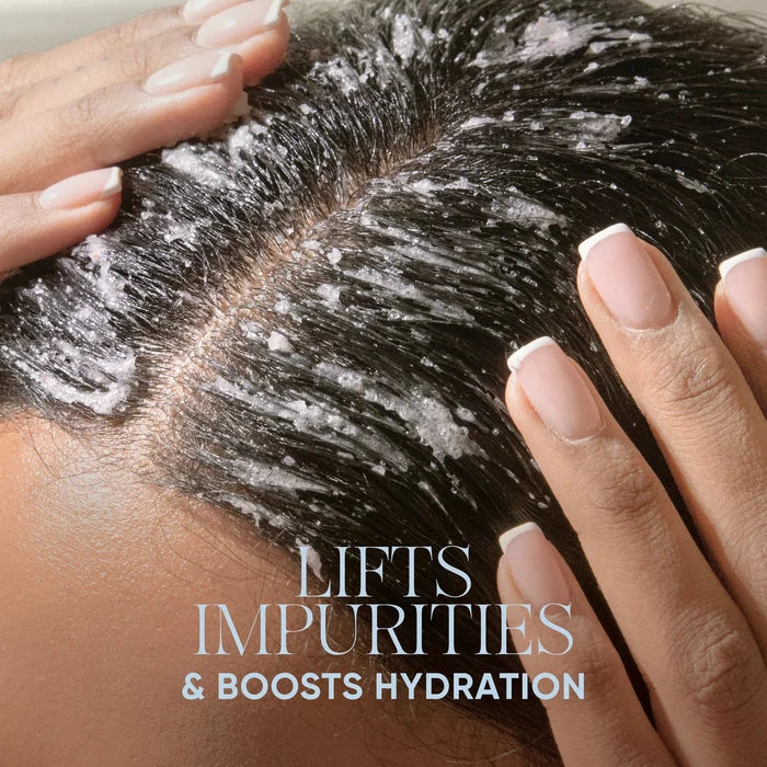 Close-up of a person's scalp with white cleansing product applied to dark hair, with both hands gently touching the hair. Text at the top reads 'SIGNATURE SENSES POWERED BY BIOTECH ACTIVES' and text at the bottom reads 'LIFTS IMPURITIES & BOOSTS HYDRATION'.