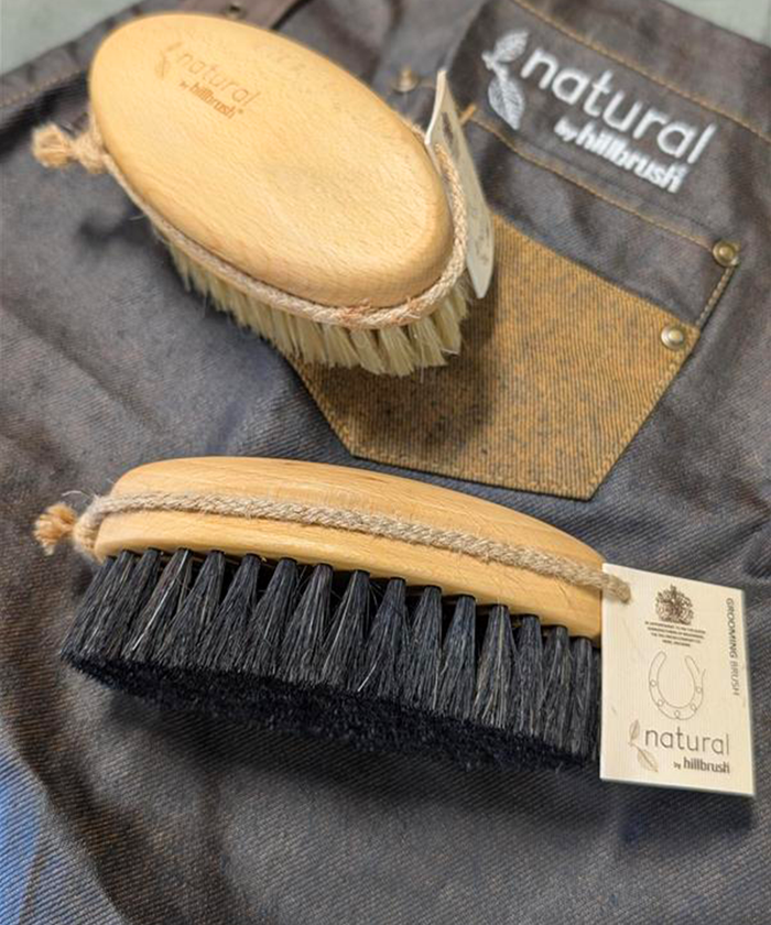 Two brushes with natural bristles on a denim background, featuring the 'natural by hillbrush' brand.