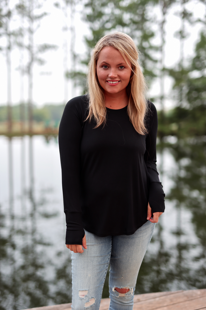 Women’s black long-sleeve ribbed top, soft fabric, casual fit, paired with distressed light jeans.