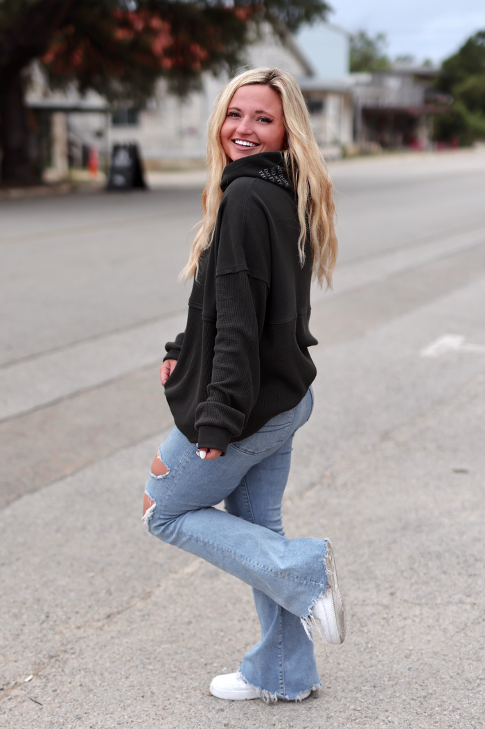 Woman in a black oversized hoodie and flared light blue jeans, smiling outdoors.