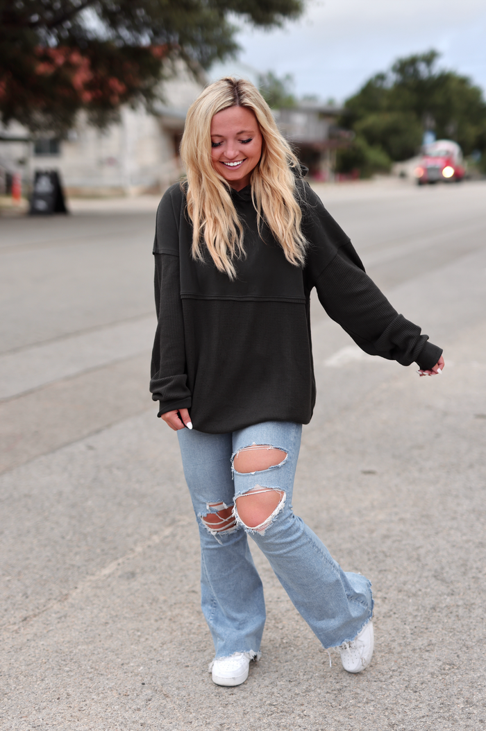 Casual women's outfit featuring a black oversized hoodie and ripped light blue jeans with stylish white sneakers.
