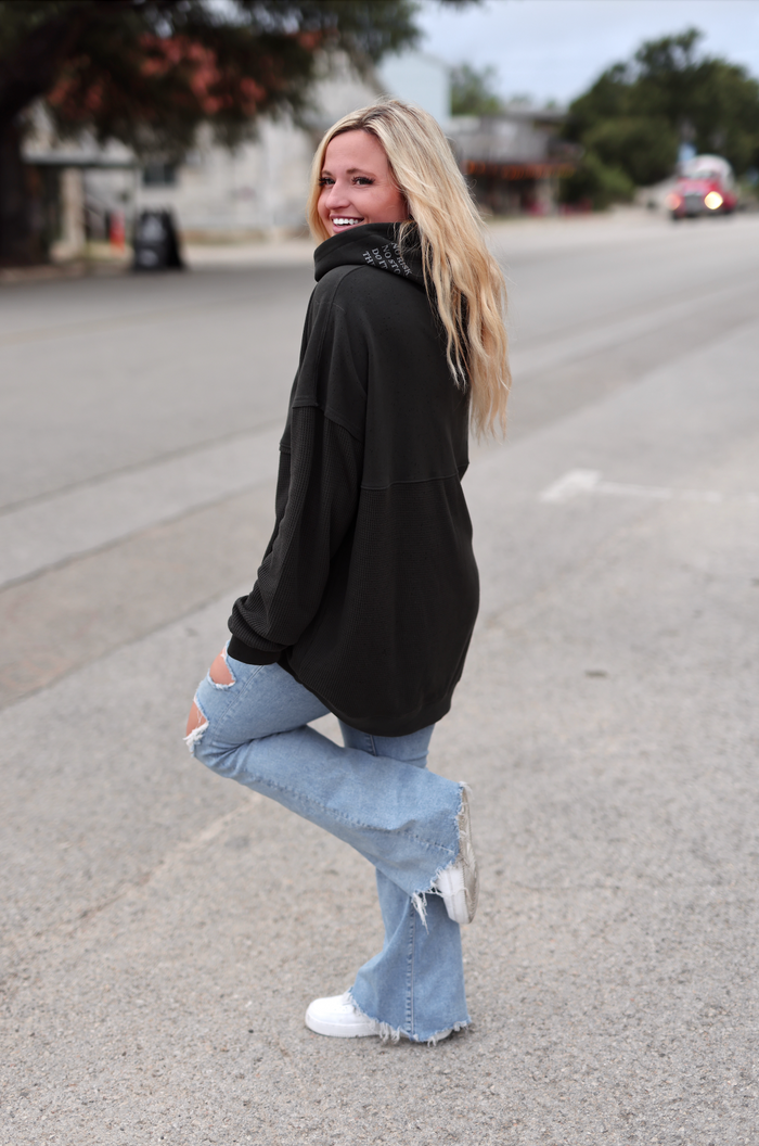 Women's oversized black sweatshirt paired with light distressed jeans and white sneakers, casual street style.