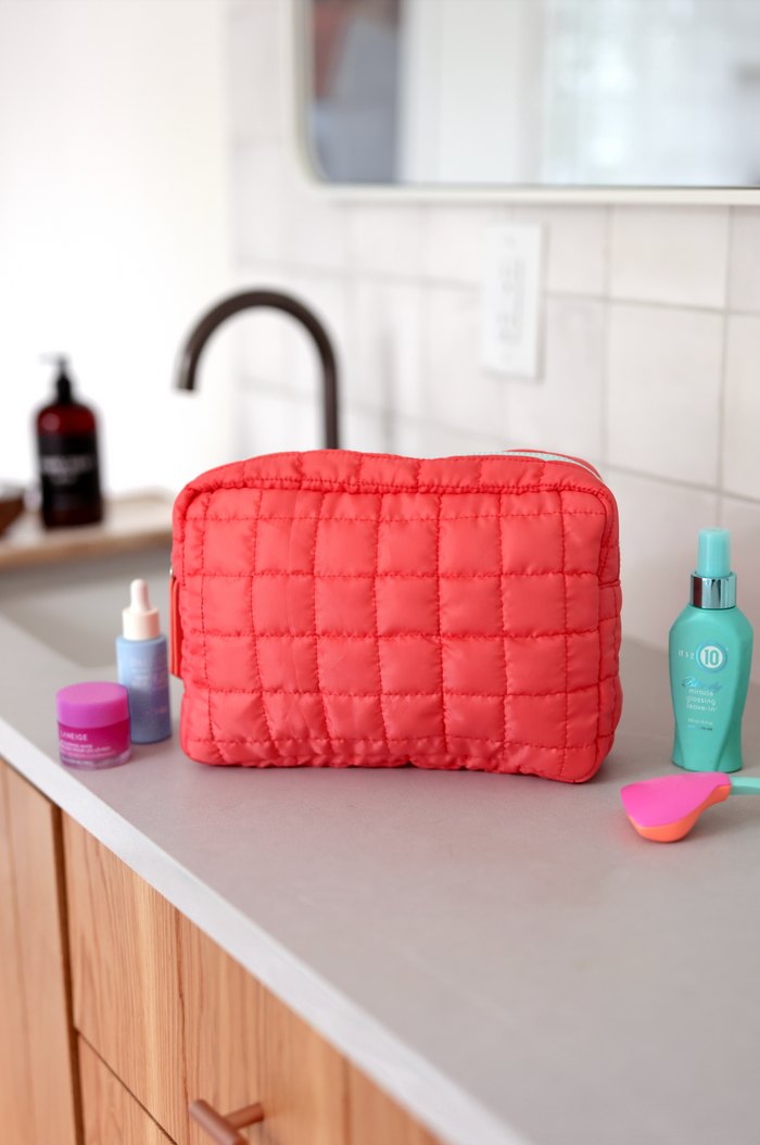 Coral quilted cosmetic bag with space for skincare products on a countertop.
