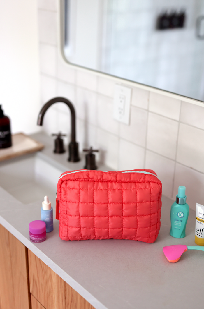 Coral quilted cosmetic bag with a zipper, perfect for organizing skincare products.