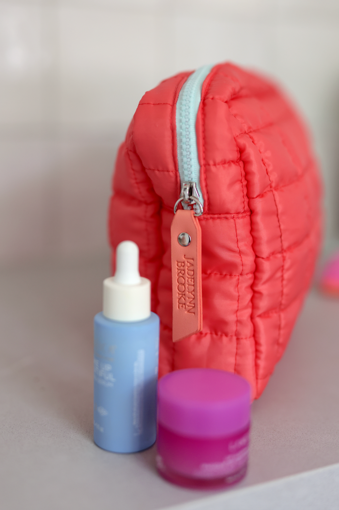 Coral quilted makeup pouch with mint zipper, accompanied by blue serum and pink cream.